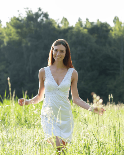 glimlachend meisje dat naar beneden kijkt en door een veld met hoge grassen en planten wandelt. foto door Bloom Photography