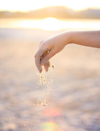 hand laat zand vallen tijdens een zonsondergang 