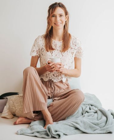 lachend meisje die zit op deken met kopje in haar handen